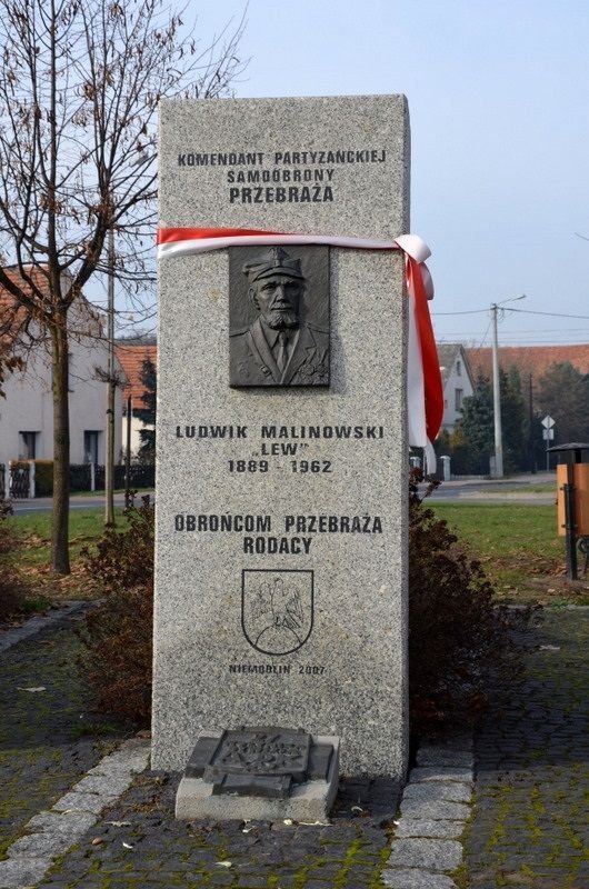 Zdjęcie przedstawiające pomnik z wizerunkiem mężczyzny. Pomnik przewiązany biało-czerwoną szarfą
