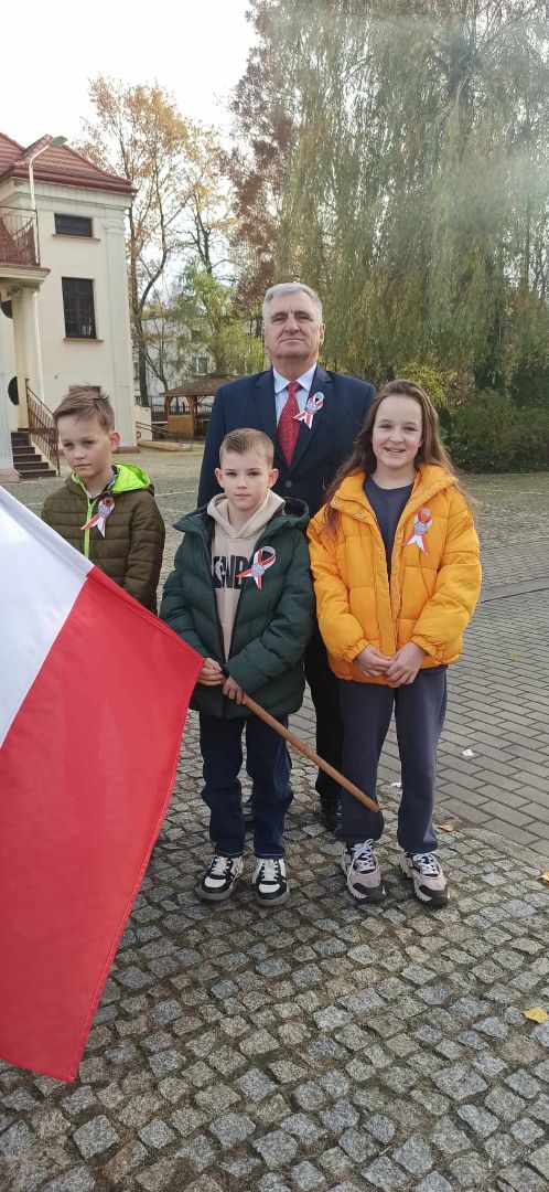 Wójt gminy stoi z 3 dzieci przy Domu Kultury. Jeden z chłopców trzyma flagę Polski