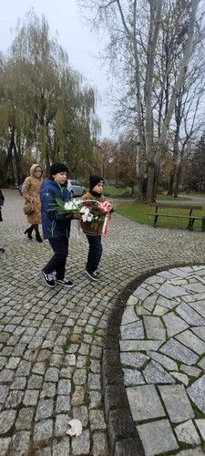 Dwoje dzieci podąża z kwiatami by je złożyć przed pomnikiem.