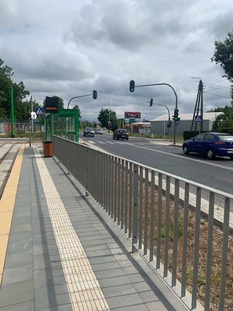 Skrzyżowanie z sygnalizacją świetlną, cztery samochody osobowe po lewej stronie widoczny przystanek tramwajowy.