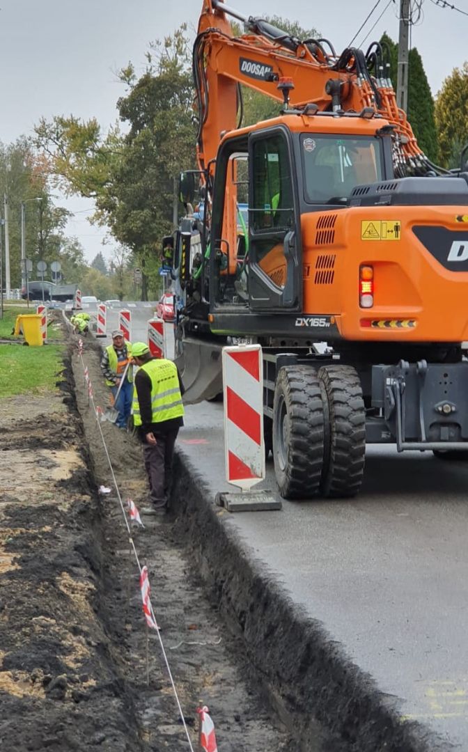 Wykopany rów po lewej strony drogi, po prawej stronie stoi samochód specjalistyczny.