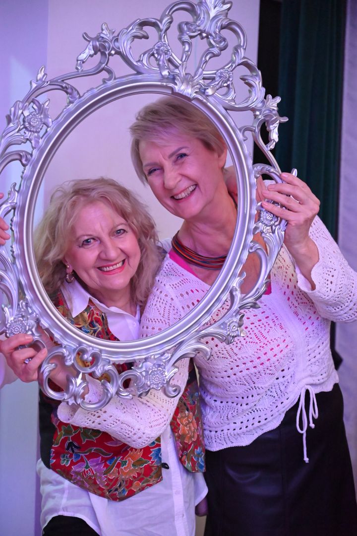 dwie kobiety pozują do zdjęcia trzymając ramkę