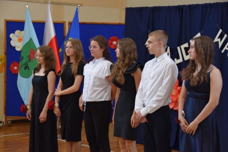 Pięć dziewcząt w czarnych sukienkach i dwóch chłopców w białych koszulkach stoją w rzędzie