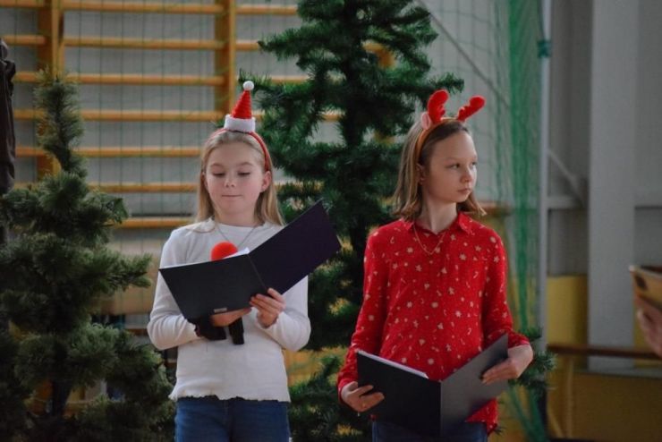 Dwie dziewczynki w świątecznych strojach. Obie trzymają mikrofony i podkładki z tekstem do czytania
