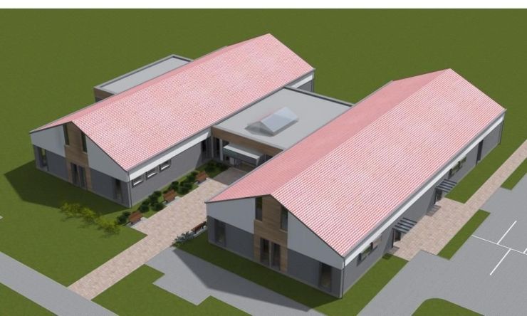 Wizualizacja budynku nowego ośrodka zdrowia przedstawiająca budynek z lotu ptaka. Piętrowy budynek w kształcie litery H z szarą elewacją i czerwonym dachem