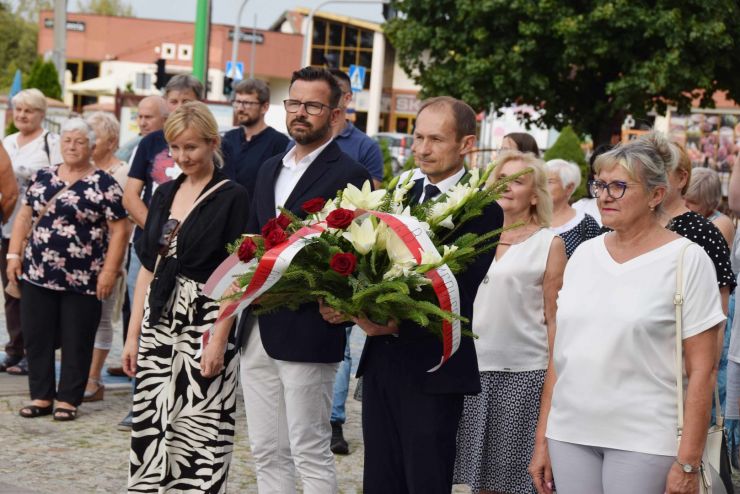 W pierwszym rzędzie mężczyzna z wiązanką biało-czerwonych kwiatów. W tle uczestnicy wydarzenia