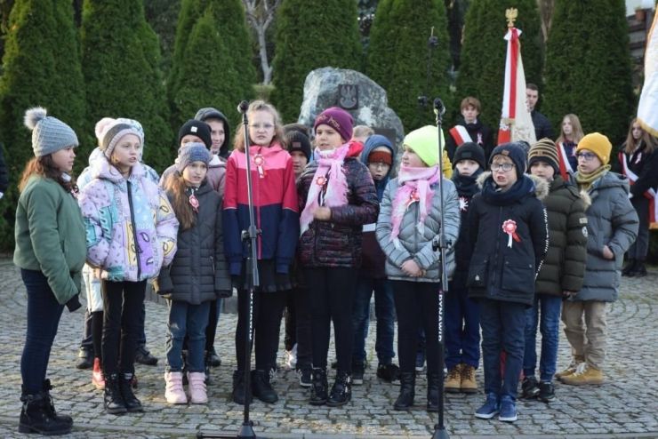 Grupa uczniów stoi przed obeliskiem i śpiewa piosenkę patriotyczną