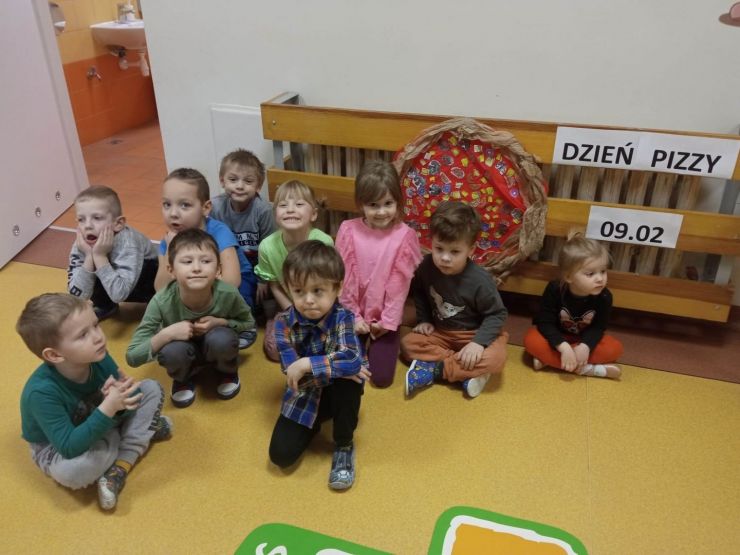 Grupa dzieci pozuje do zdjęcia obok własnoręcznie wykonanej pizzy z kartonu