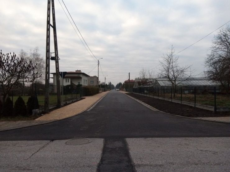 Ulica z nowym asfaltem po lewej stronie chodnik po prawej nowe ogrodzenie posesji.