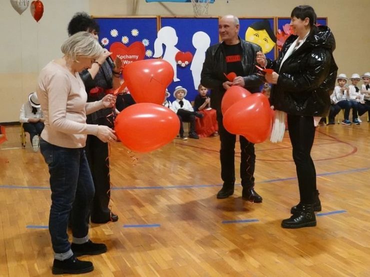 Cztery osoby stoją w rzędzie. Wszyscy trzymają czerwone balony w kształcie serca