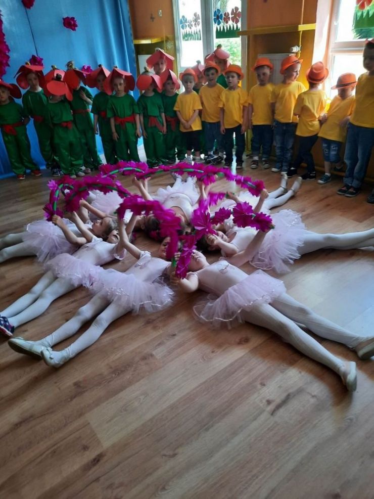 Grupa dziewcząt przebranych za baletnice leży na podłodze w okręgu.