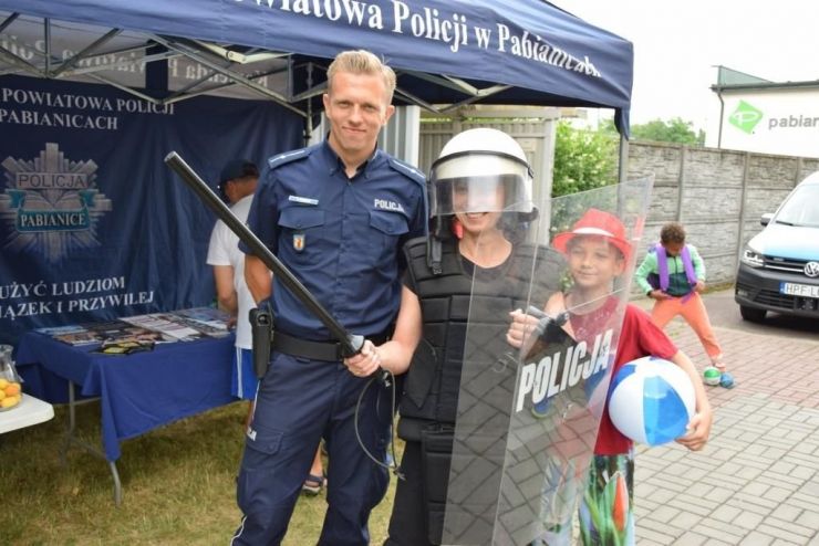Kobieta w bojowym ubraniu policyjnym stoi obok policjanta. Obok stoi chłopiec w czerwonym kapeluszu