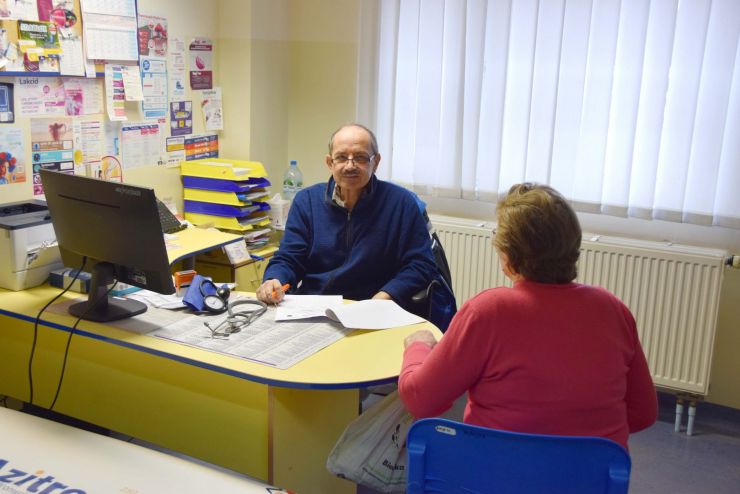 Lekarz siedzi za biurkiem na obok biurka na krześle siedzi pacjent.