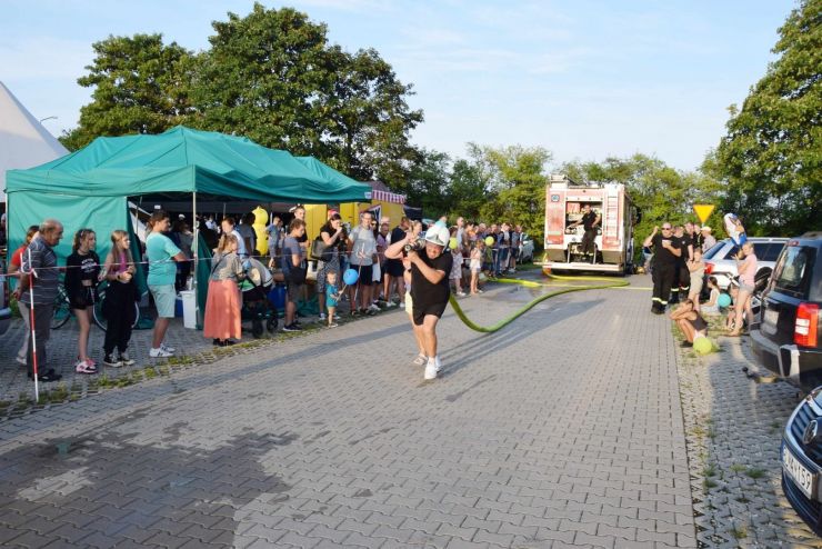 Uczestnik konkursu OSP biegnie z wężem strażackim. W tle za taśmą publiczność