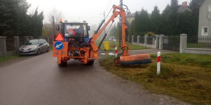 Pomarańczowy ciągnik wykasza pobocze ulicy