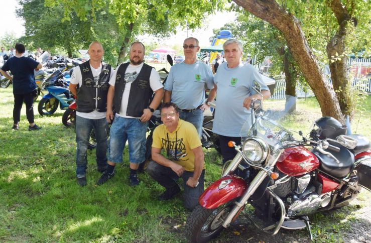 Na zdjęciu wójt gminy w błękitnej koszulce z herbem gminy. Obok motocykliści i motocykl.