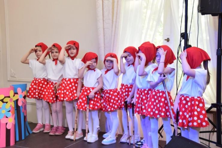 Grupa dziewczynek ubranych w czerwone spódniczki i chustki. Dziewczynki stoją na scenie.