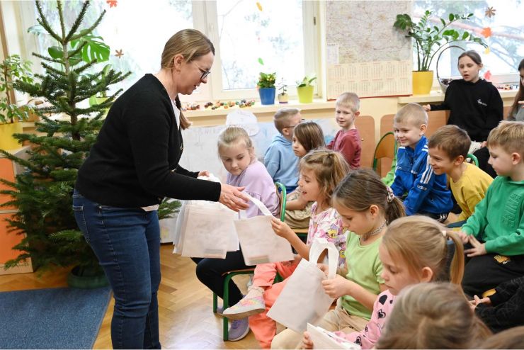 kobieta rozdaje torebki siedzącym przedszkolakom