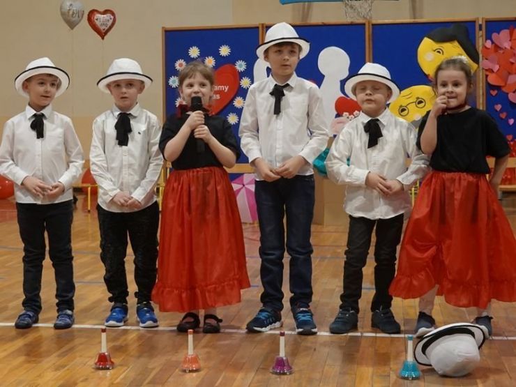 Grupa dzieci - chłopcy ubrani w białe koszule i kapelusze, dziewczynki w czerwonych sukienkach.
