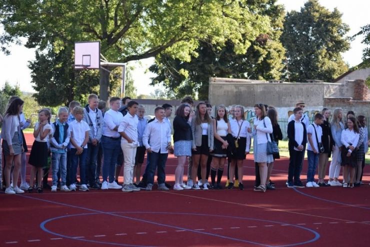 Grupa dzieci ubranych na galowo stoi na boisku podczas rozpoczęcia roku szkolnego
