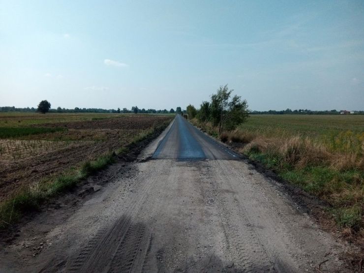 Na środku droga utwardzona przechodząca w nakładkę asfaltową. Po prawej i lewej stronie widoczne pola.