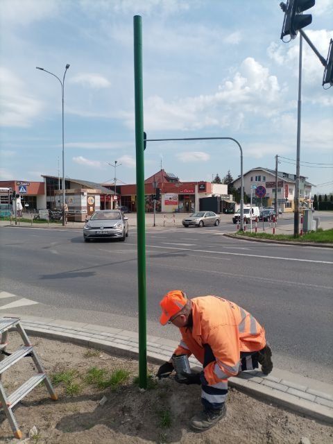 Pracownik maluje na zielono słup na którym zawiesi nazwę ulicy.