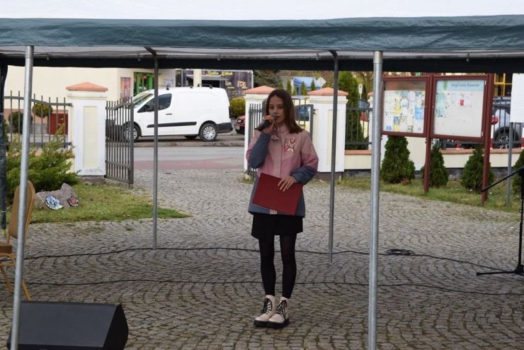 Dziewczyna w różowej kurtce trzyma w ręku mikrofon i recytuje wiersz patriotyczny