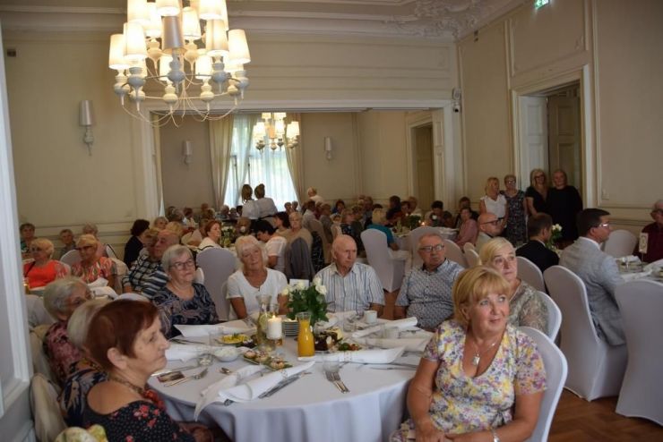 Na sali z kryształowymi żyrandolami, przy okrągłych stołach siedzą uczestnicy spotkania