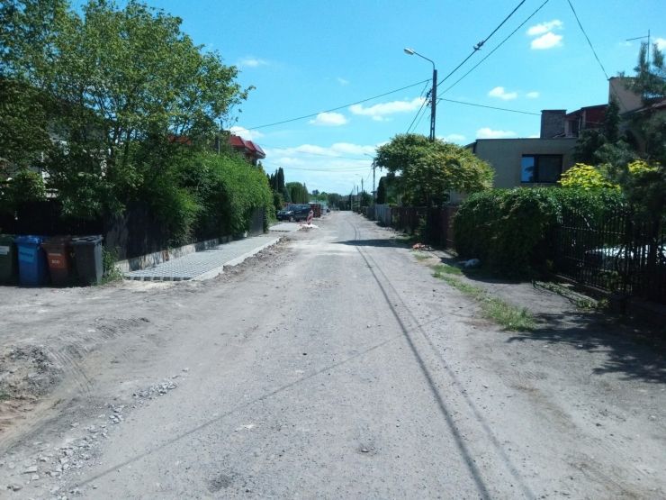Droga z zerwanym asfaltem po lewej stronie  chodnik w trakcie budowy.