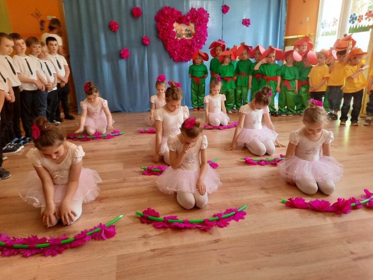 Dziewczęta przebrane w stroje baletnic klęczą na podłodzie. Przed każdą z nich leżą różowe kwiaty - akcesoria