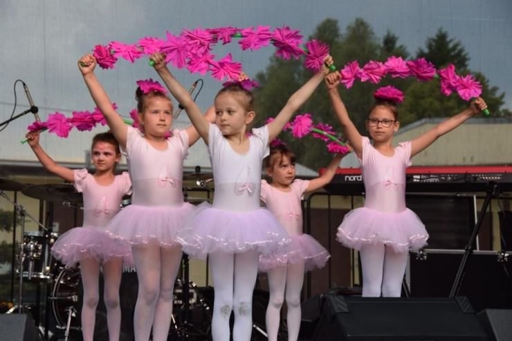 Grupa dziewcząt ubranych w stroje baletnic stoi na scenie