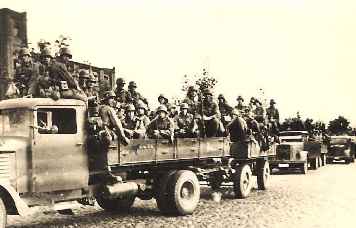 Czarno-białe zdjęcie przedstawiające ciężarówki z żołnierzami i bronią
