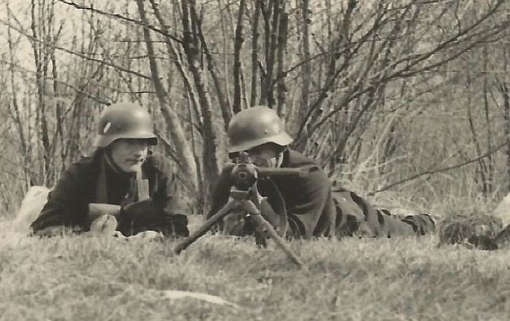 Zdjęcie w sepii przedstawiające dwóch żołnierzy z karabinami leżących na trawie. W tle widoczne drzewa