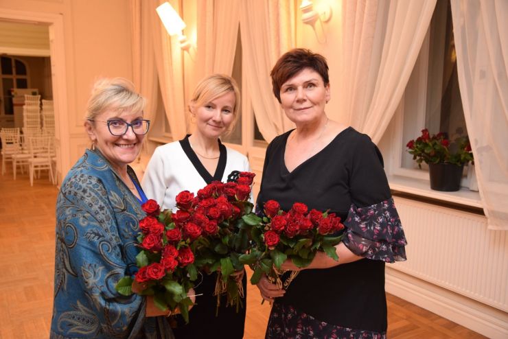  Trzy kobiety pozują do zdjęcia trzymając naręcza róż.