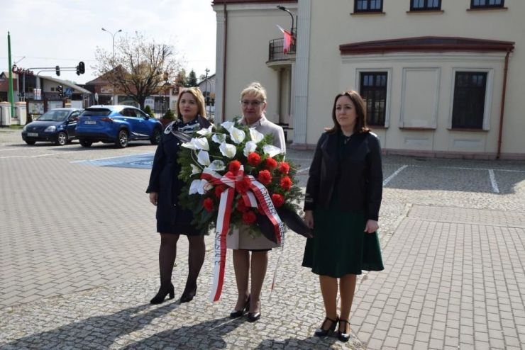 Trzy kobiety stoją przy Gminnym Domu Kultury z Biblioteką w Ksawerowie. Jedna z kobiet trzyma wieniec kwiatów