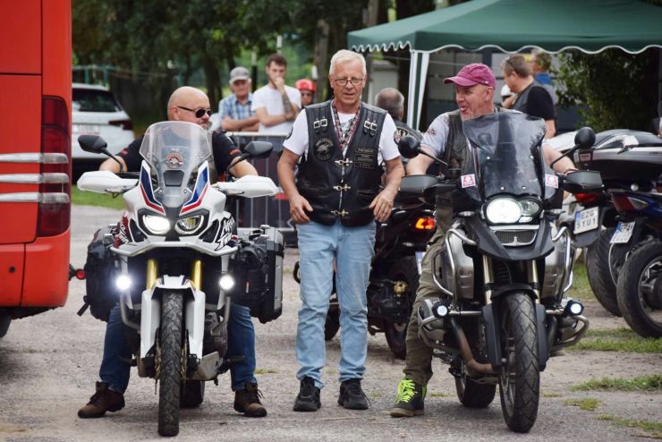 Obok mężczyzny ubranego w skórzaną kamizelkę stoją dwa motocykle. Kierowcy przygotowują się do konkursu.